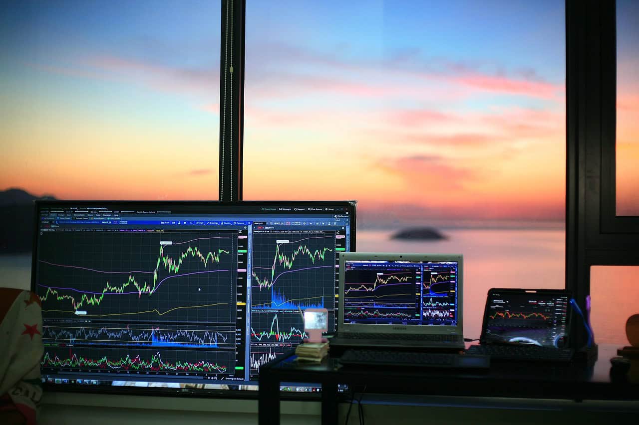 High-tech trading setup with multiple monitors displaying stock market charts, during sunset by the window.